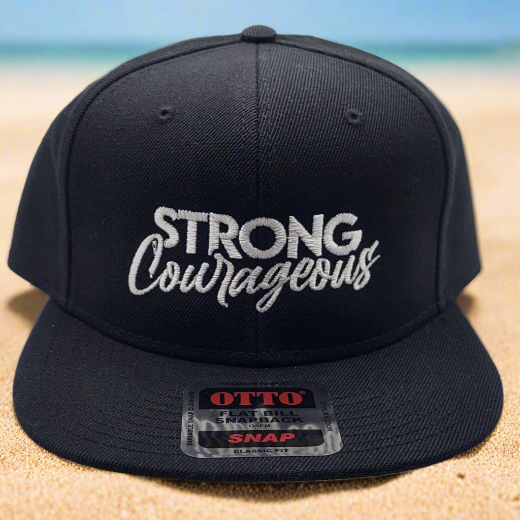 Black flat bill cap with 'STRONG Courageous' text in white on the front, with a gray undervisor and a label showing the brand WikaWear.